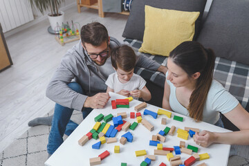Fototapeta premium Mother and father playing with their cute smart toddler son at home using colorful wooden toys