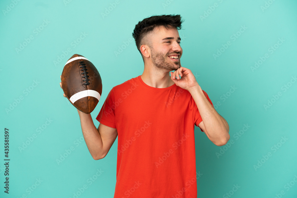 Wall mural Young Caucasian man playing rugby isolated on blue background thinking an idea while looking up