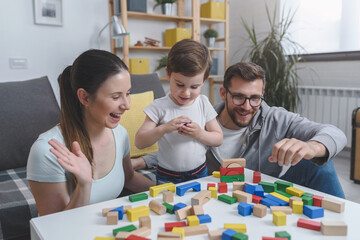 Mother and father playing with their cute smart toddler son at home using colorful wooden toys