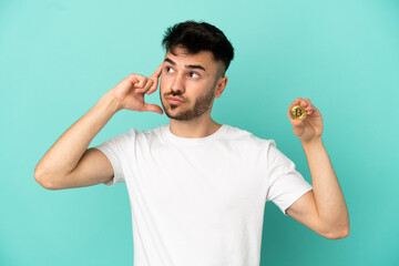 Young man holding a Bitcoin isolated on blue background having doubts and thinking