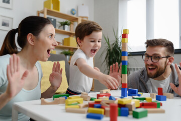 Mother and father playing with their cute smart toddler son at home using colorful wooden toys