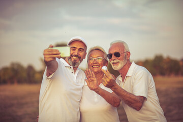 Senior golfers using phone and taking self portrait. Focus is on background.  Happy golfers having a video chat over smart phone