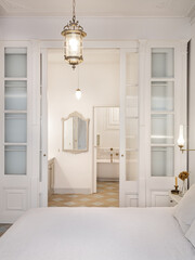 Interior of retro or classic style bedroom with vintage chandelier. View to bathroom decorated in beige color with bath zone