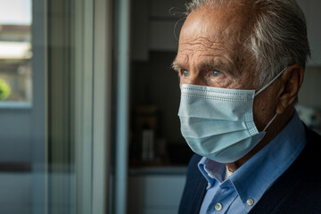 Cinematic close up shot of an elderly thoughtful man wearing protective medical mask is looking...