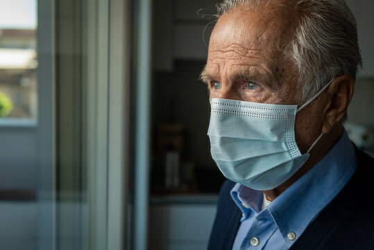 Cinematic close up shot of an elderly thoughtful man wearing protective medical mask is looking through a window. Concept of healthcare, protection, virus transmission, breathing, quarantine,covid-19.