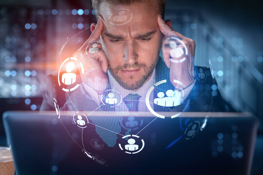 Handsome businessman in suit at workplace working with laptop to hire new employees for international business consulting. HR, social media hologram icons over office background