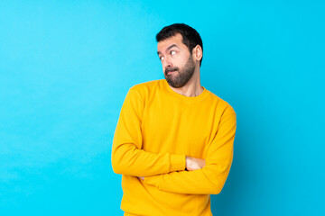 Young caucasian man over isolated blue background making doubts gesture looking side