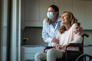 Cinematic shot of social worker with medical mask taking care of senior woman in wheelchair while...