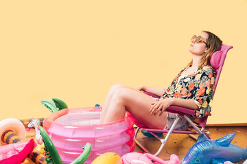 unknown woman in summer clothes sitting on a pink chair with her feet in a children's poo, with a lot of inflatables on the floor around her.