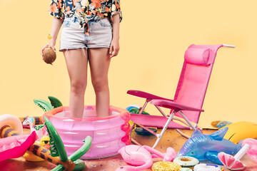 unknown woman in summer clothes holding a coconut cocktail in a children's pool, with a lot of inflatables on the floor around her.