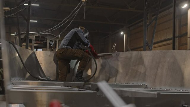 Wide shot of unrecognizable shipyard worker wearing helmet, welding new metal boat in industrial premises