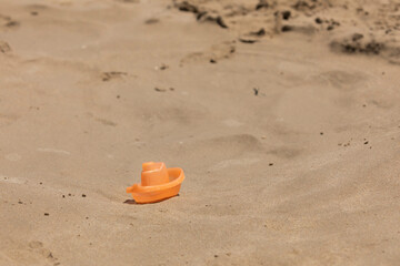 Fototapeta na wymiar A small toy boat, belonging to a child, lies forgotten in the wet sand, near the shore, on the beach of Torrenostra, Mediterranean Sea, Castellon province, Spain.