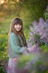Photo of a girl with long hair near a lilac bush.
