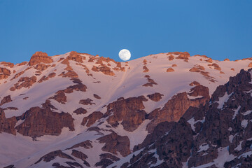 The moon rises due to high snow mountains in spring