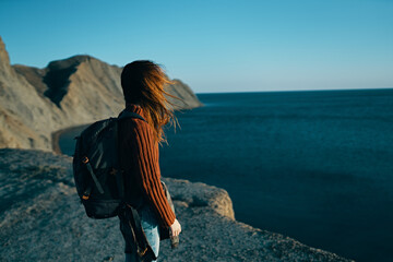 woman in a sweater in nature near the sea with a backpack on her back