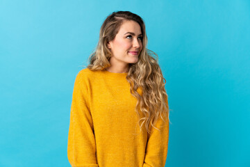 Young Brazilian woman isolated on blue background having doubts while looking up