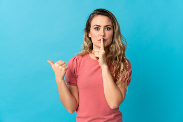 Young Brazilian woman isolated on blue background pointing to the side and doing silence gesture