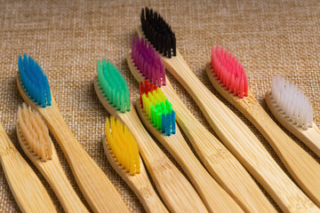 Bamboo toothbrushes with colorful bristles lie diagonally on the burlap
