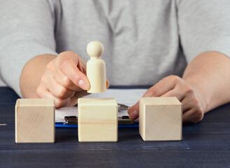 female hand holds a wooden figurine of a man and puts on a cube