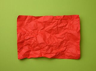 crumpled rectangular sheet of red paper on a green background, top view