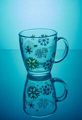 Mug with mirror reflection .The mug stands with a blue background. There are snowflakes painted on the mug 