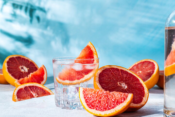 refreshing cocktail with grapefruit on a blue background. a glass glass with ice and grapefruit slices sits on the table among the sliced citrus fruits