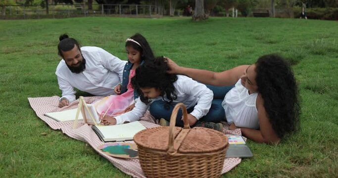Indian parents having fun at city park painting with children doing picnic - Family, summer and love concept 