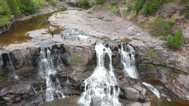 Aerial clip panning up Gooseberry waterfalls. Waterfalls surrounded by rocky landscape and forested area. Near Duluth, MN. Outdoors, summer.