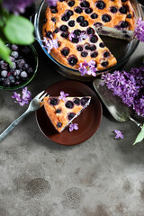 Obraz na płótnie Canvas Cottage cheese casserole with blueberries in a glass baking dish on the table with a bouquet of blooming lilacs.
