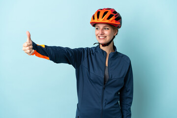 Young cyclist woman isolated on blue background giving a thumbs up gesture