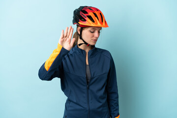 Young cyclist woman isolated on blue background making stop gesture and disappointed - obrazy, fototapety, plakaty