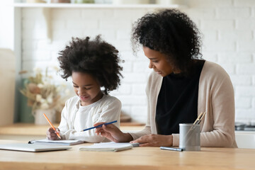 Loving young African American mother help little biracial daughter with homework assignment at...