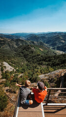 Two boys sitting over the cliff and enjoing the beautiful view of the mountains. Vertical.