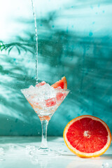 refreshing cocktail with grapefruit on a green background. a glass with ice and pieces of grapefruit is on the table in which the liquid is poured on top