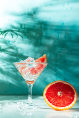 refreshing cocktail with grapefruit on a green background. a glass with ice and pieces of grapefruit is on the table in which the liquid is poured on top