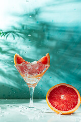 refreshing cocktail with grapefruit on a green background. a glass with ice and pieces of grapefruit is on the table in which the liquid is poured on top