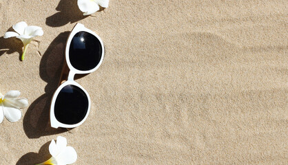 Fototapeta na wymiar Sunglasses with white plumeria flower on sand. Summer background concept.