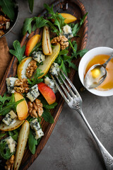 Salad with gorgonzola, rucola, pears, walnuts and honey in a long  wooden plate. Healthy eating. Cheese with a noble blue mold on a gray table and
dark background. Healthy eating. Light dinner.
