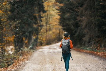 woman with backpack on the road in the forest in autumn landscape tall trees model