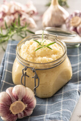 Aromatic garlic paste in a glass jar laid on rustic kitchen cloth with bulbs and peeled cloves and rosemary