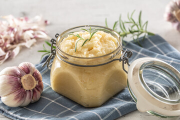 Aromatic garlic paste in a glass jar laid on rustic kitchen cloth with bulbs and peeled cloves and...