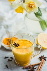 A beautiful glass with golden milk, turmeric, spices and lemon on a gray background. Healthy Ayurvedic drink. Strengthening the immune system. Antioxidant and superfood