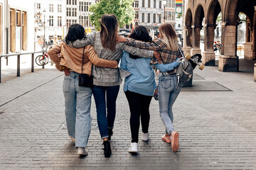 Back view of four friends hugging and walking in city center. urban lifestyle