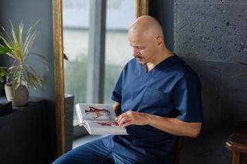 A massage therapist in a blue suit reads a book on human anatomy in his cozy office