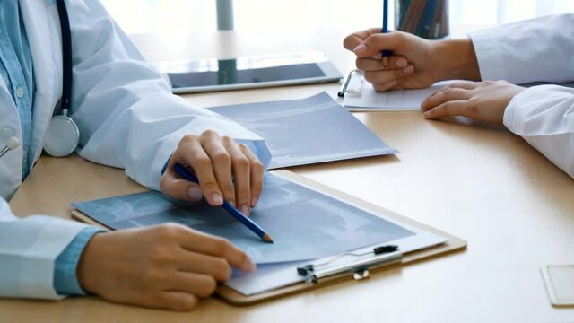 Two women doctors consulting diagnostics using x-ray film at hospital medicare treatment clinic. Doctor writing prescription for medical healthcare oncologist therapy using laptop. Healthcare concept