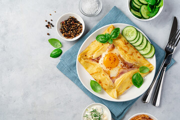 Egg, ham and cheese are wrapped and fried in a pancake and decorated with basil and fresh cucumber on a gray background. - obrazy, fototapety, plakaty