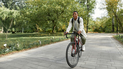 Naklejka premium Man with backpack riding bike along park alley