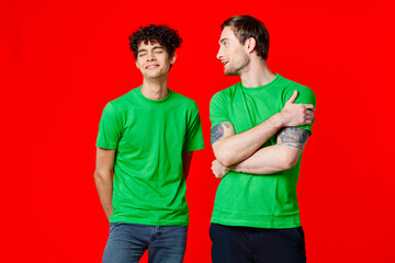 joyful friends in green t-shirts are standing next to red background