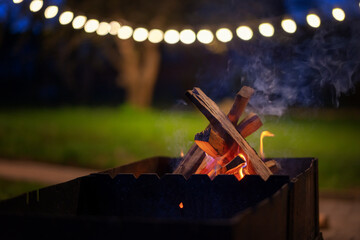 Wooden logs burning in the grill in the night garden decorated with lanterns. summer parties with...