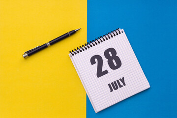 July 28th. Day 28 of month, calendar date. Notebook with a spiral and pen lies on a yellow-blue background